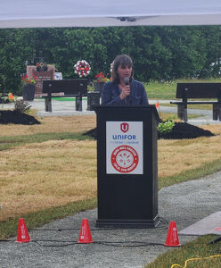 Janice Martell stands at a podium in the park and speaks at the ceremony.